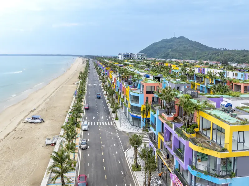 Con đường ven biển dọc bãi cát Hải Tiến, bên phải là dãy nhà nhiều màu của Flamingo Hải Tiến, cuối đường là núi trên mũi Linh Trường