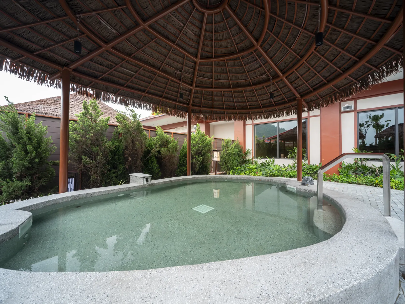 Bể onsen ngoài trời hình bầu dục dưới mái lá ở Flamingo Tân Trào, quanh là cây xanh