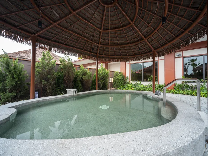 Bể onsen ngoài trời hình bầu dục dưới mái lá ở Flamingo Tân Trào, quanh là cây xanh