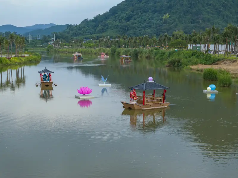 Mặt sông Phó Đáy phẳng lặng trước Flamingo Tân Trào, có thuyền mái ngói và đèn hoa sen nổi trên nước, phía sau là đồi xanh