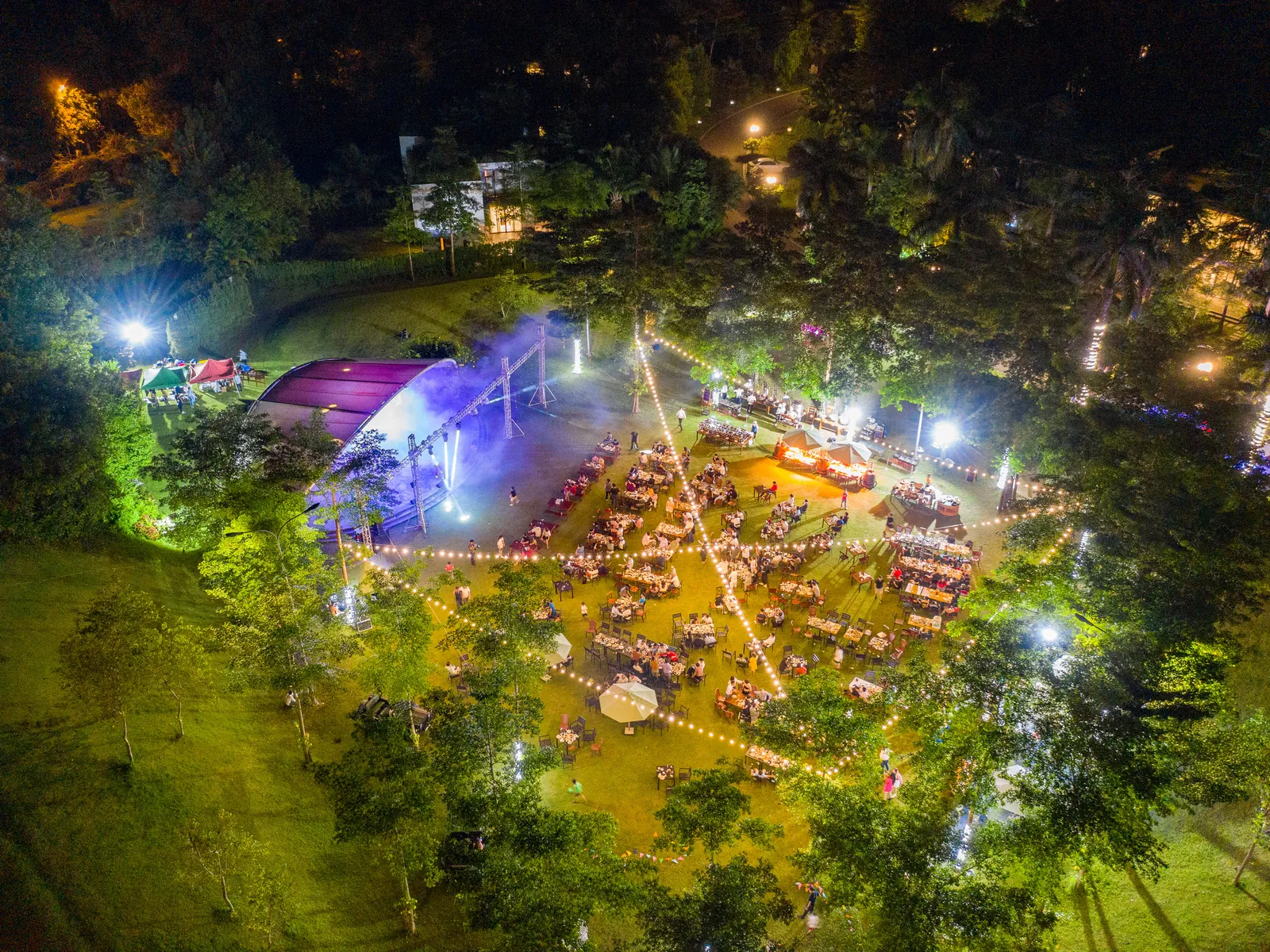 Tiệc gala ngoài trời buổi tối giữa rừng cây ở Flamingo Đại Lải, sân khấu mái vòm và bàn tiệc lên đèn nhìn từ trên cao