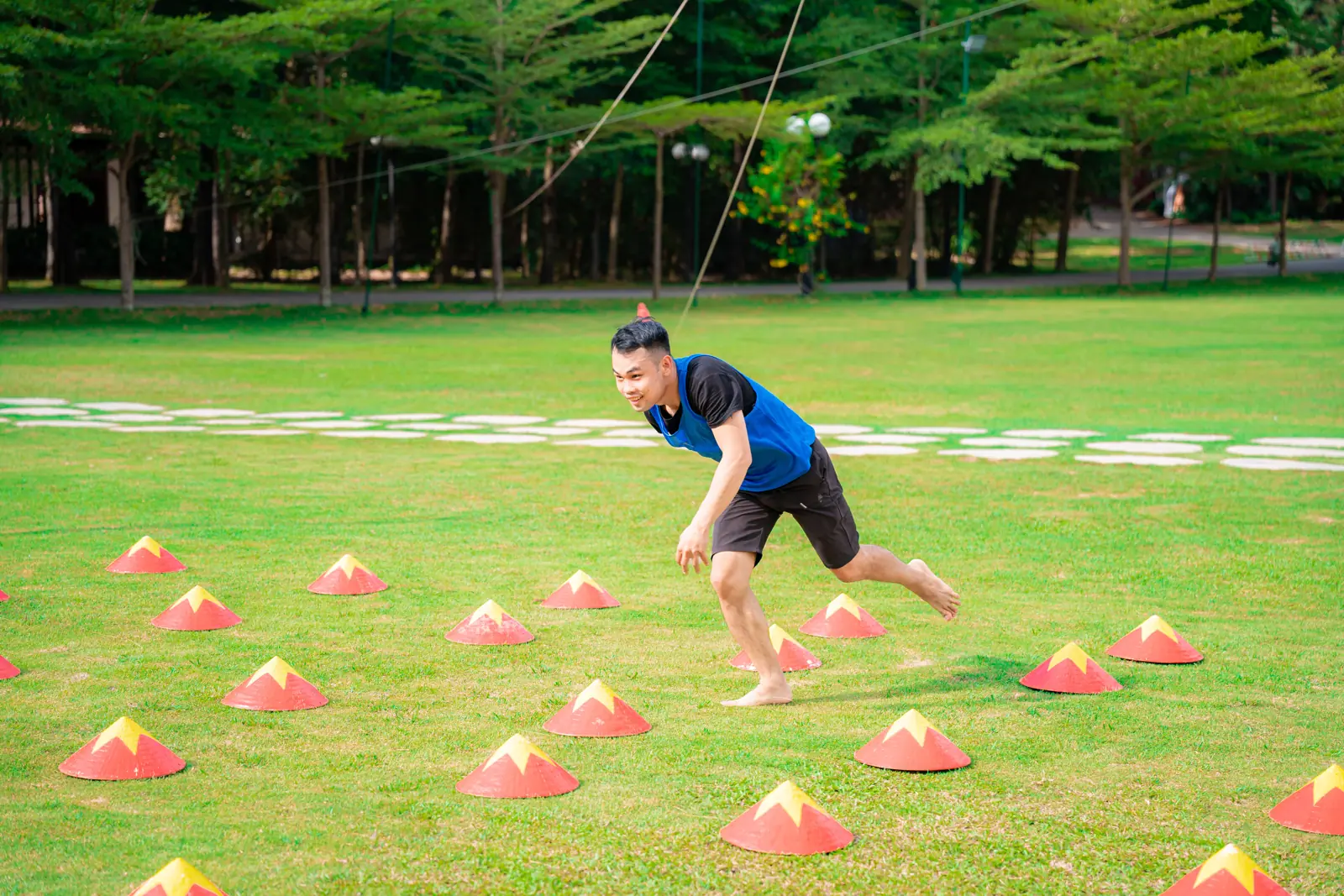 Một người chạy qua hàng nón đánh dấu trên bãi cỏ dưới rừng thông trong trò chơi teambuilding ở Flamingo Đại Lải