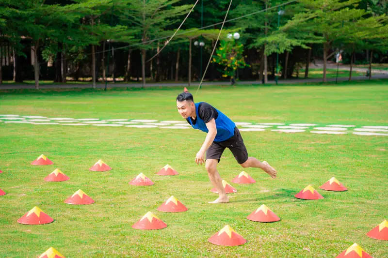 Một người chạy qua hàng nón đánh dấu trên bãi cỏ dưới rừng thông trong trò chơi teambuilding ở Flamingo Đại Lải