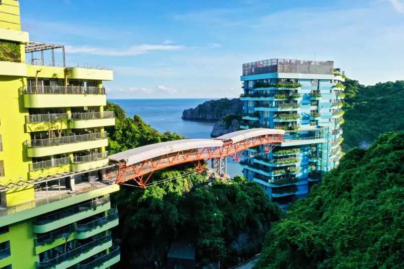Cầu Mây màu cam nối hai tòa nhà phủ cây xanh của Flamingo Cát Bà, phía sau là biển và các đảo đá