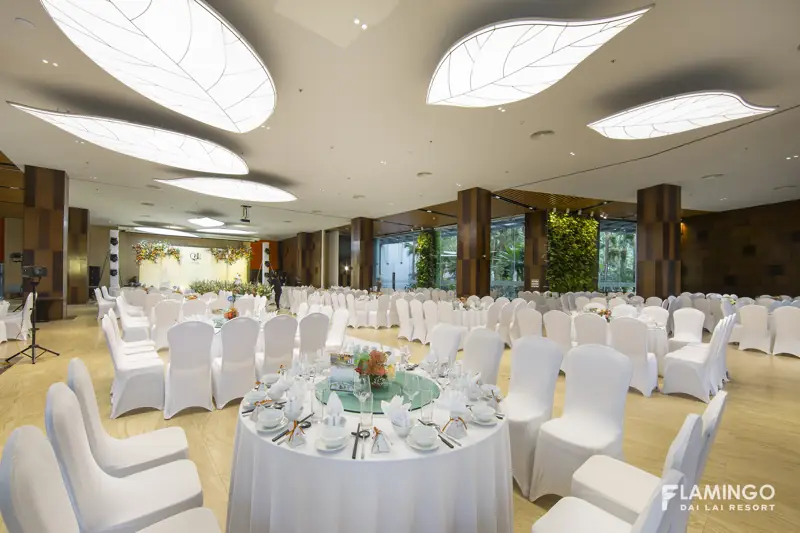 Sảnh Symphony Hall bày bàn tiệc tròn khăn trắng, trần đèn hình lá