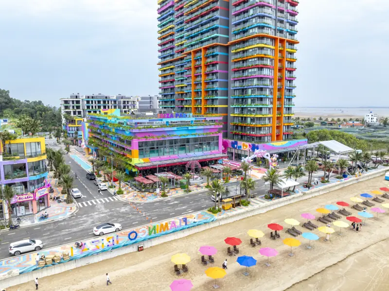 Nhìn từ trên cao bãi biển trước Flamingo Hải Tiến với hàng ô dù nhiều màu, phía sau là tòa Party Center và tòa tháp 21 tầng
