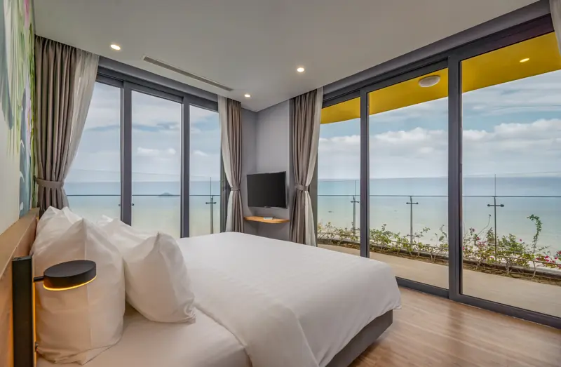 Phòng ngủ Premier Residence 01 phòng ngủ: giường đôi, vách kính và ban công nhìn ra biển