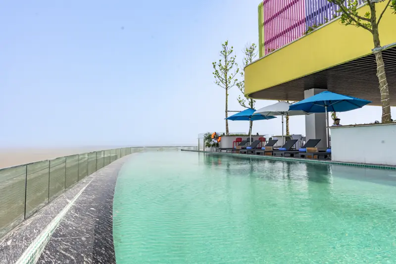 Mặt nước bể vô cực tầng 21 nối với đường chân trời biển, bên cạnh là dãy ghế nằm và ô xanh
