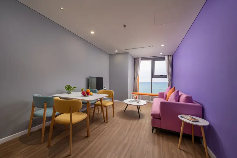 Phòng khách căn Premier Residence 2 phòng ngủ với sofa hồng, bàn ăn và cửa sổ nhìn biển