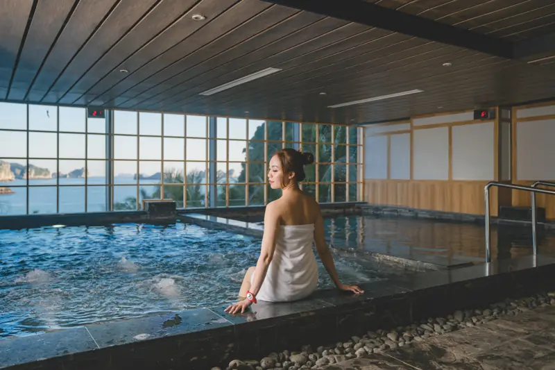 Khu onsen trong nhà ở Flamingo Cát Bà: bể sục, trần gỗ, vách kính nhìn ra biển và núi đá