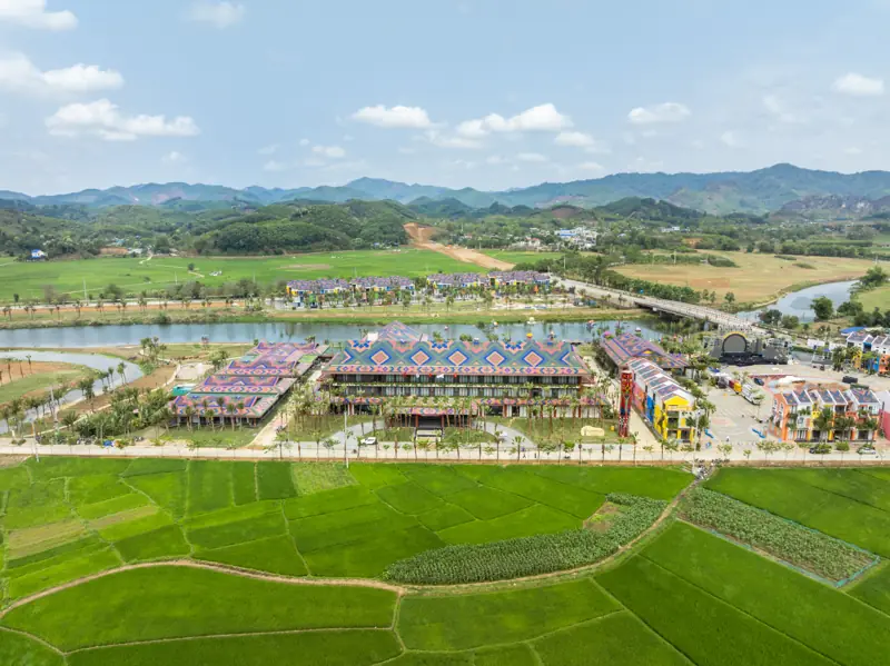 Toàn cảnh Flamingo Tân Trào Resort ban ngày: tòa khách sạn mái thổ cẩm bên sông Phó Đáy, phía trước là ruộng lúa